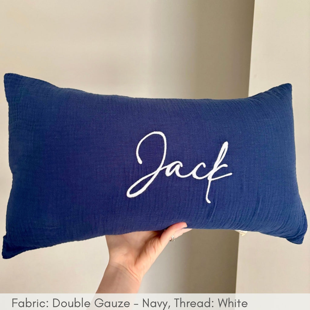 Navy blue pillow with 'Jack' embroidered on it held by a hand against a neutral background