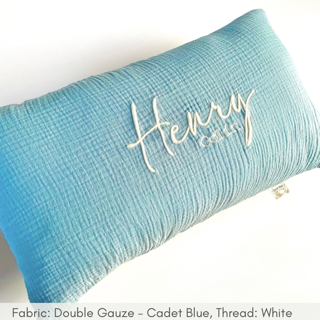 Light blue pillow with 'Henry' embroidered on it against a white background