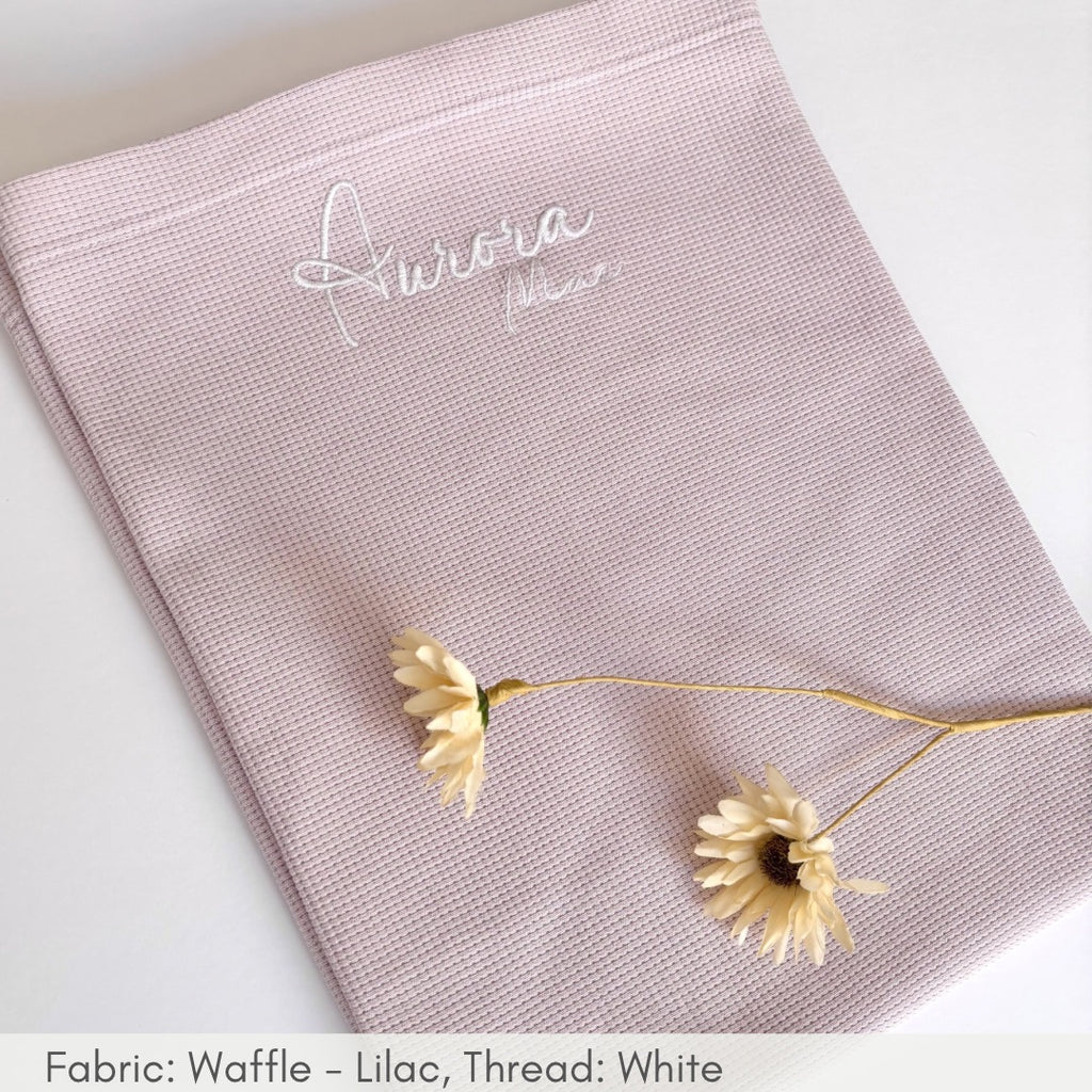 Pink waffle-textured fabric with 'Aurora' embroidery, featuring a delicate yellow flower on a white background.