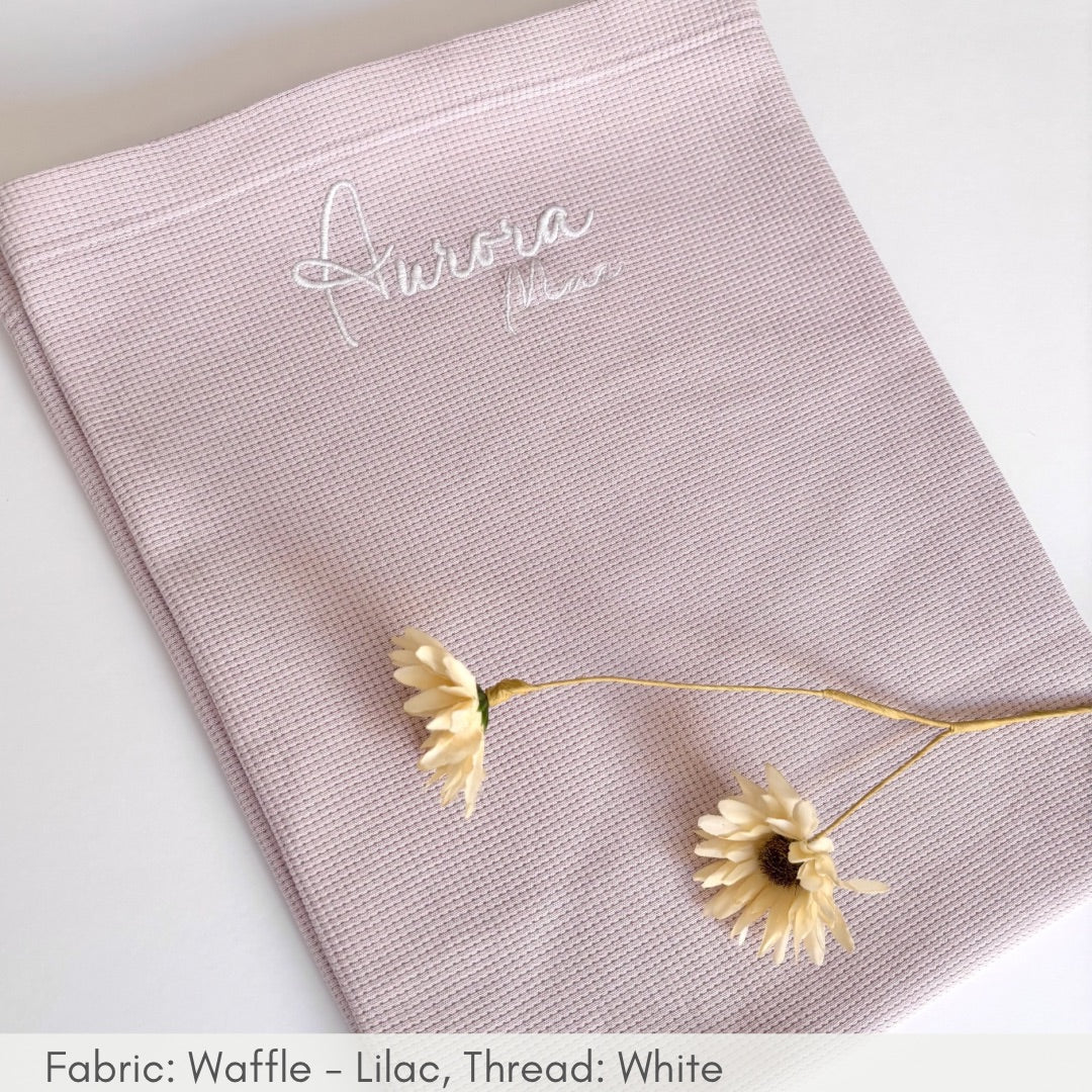 Pink waffle-textured fabric with 'Aurora' embroidery, featuring a delicate yellow flower on a white background.