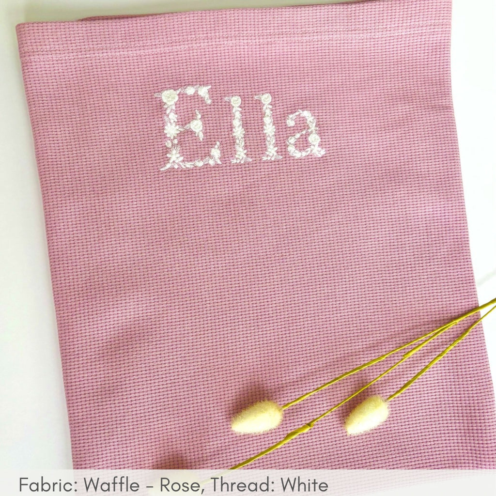 Pink fabric with 'Ella' embroidered on it, accompanied by decorative elements.