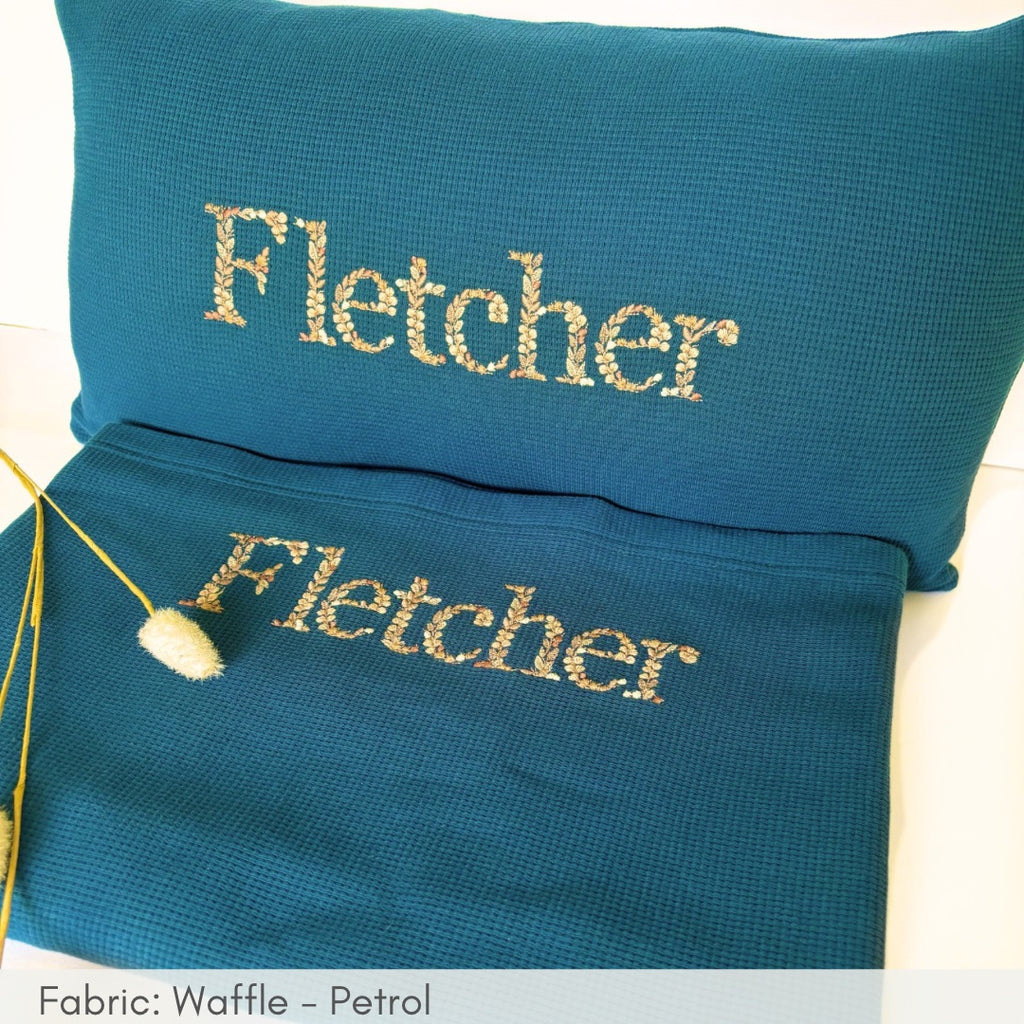 Teal pillow and pouch with 'Fletcher' embroidery on a white background