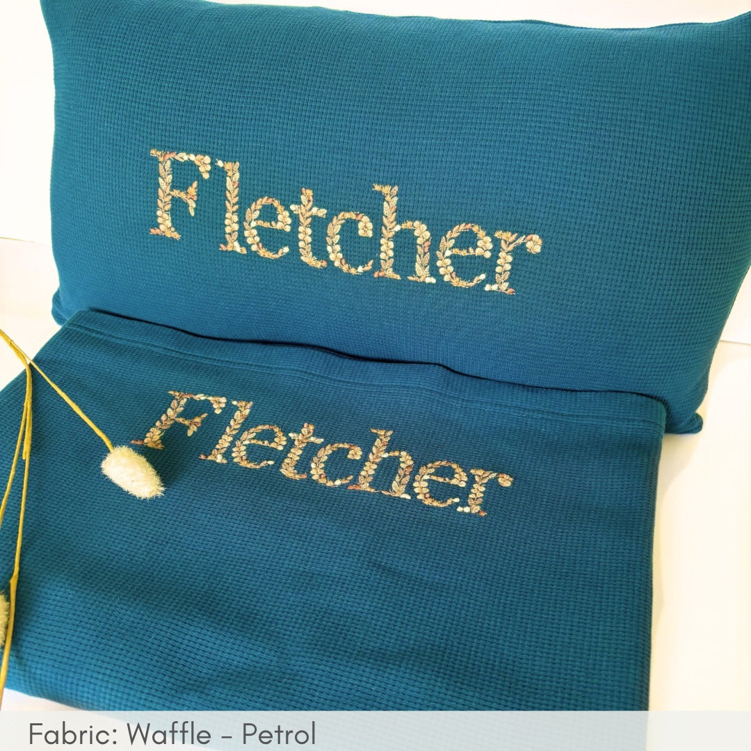 Teal pillow and pouch with 'Fletcher' embroidery on a white background