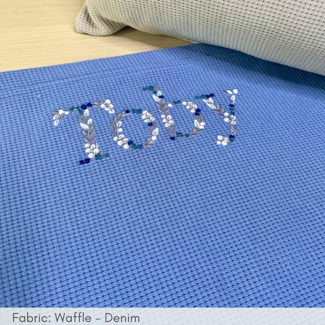 Blue cross-stitch fabric with '.Today' embroidery on a wooden surface