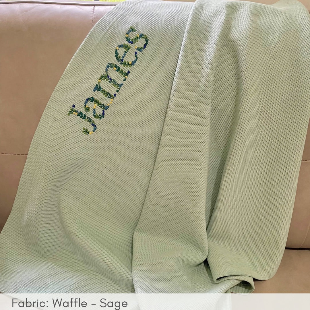 Green blanket with embroidered name 'James' on a beige surface