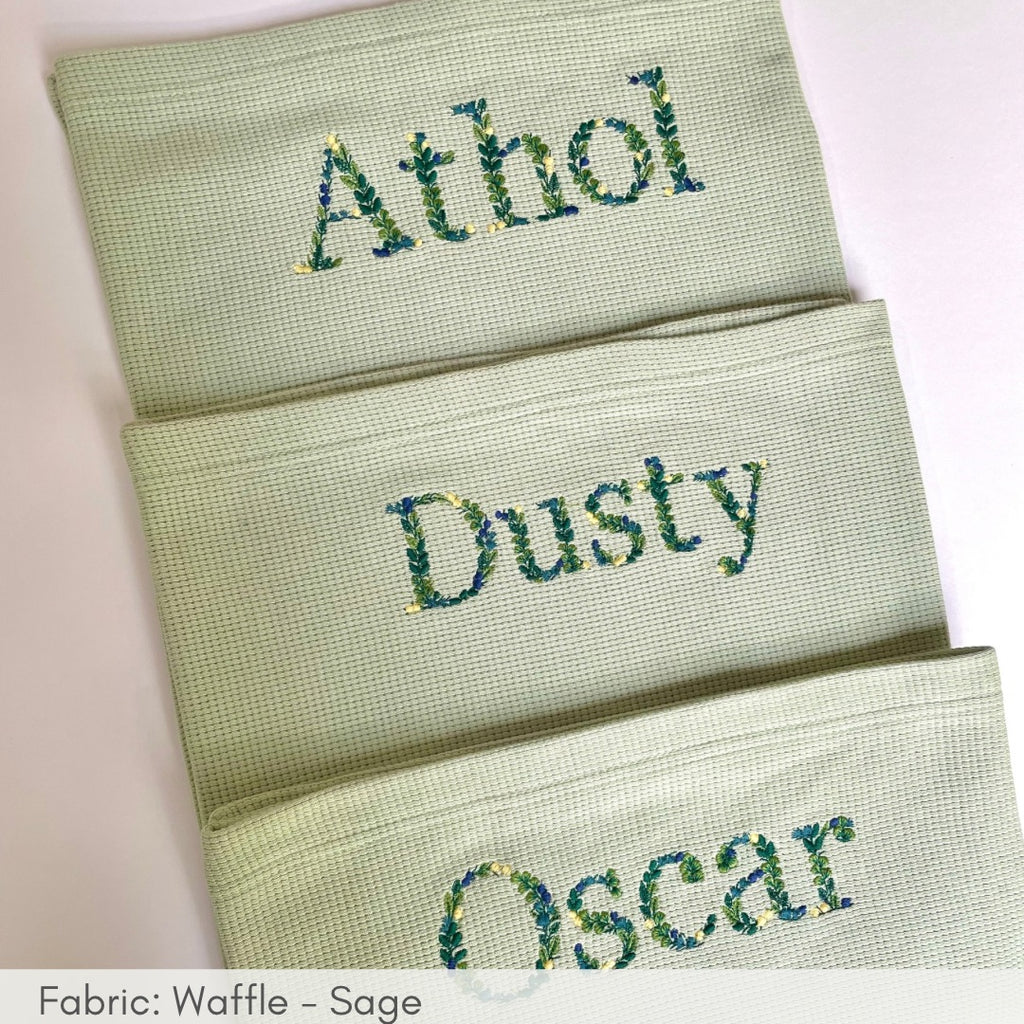 Three green towels with embroidered names on a white background