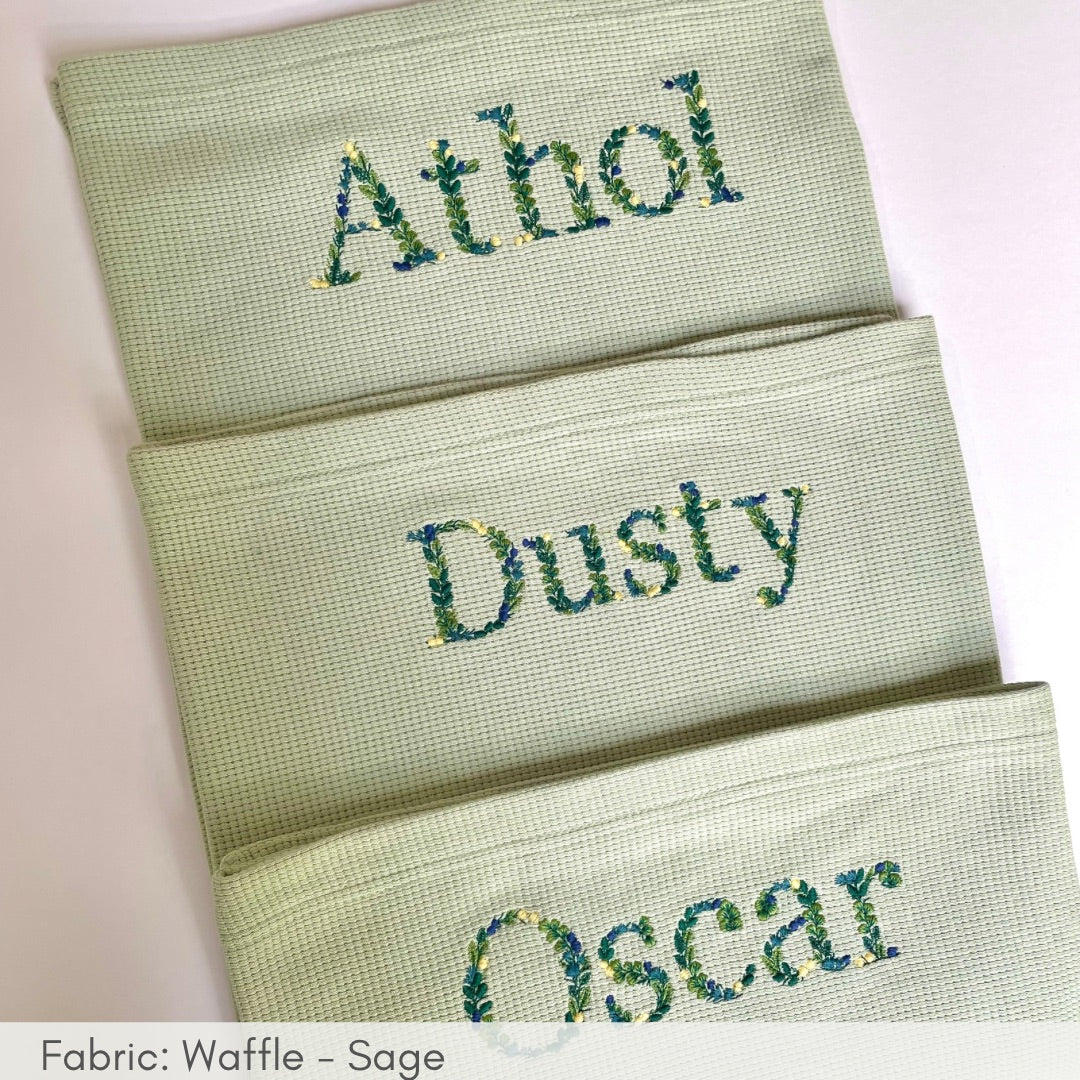 Three green towels with embroidered names on a white background